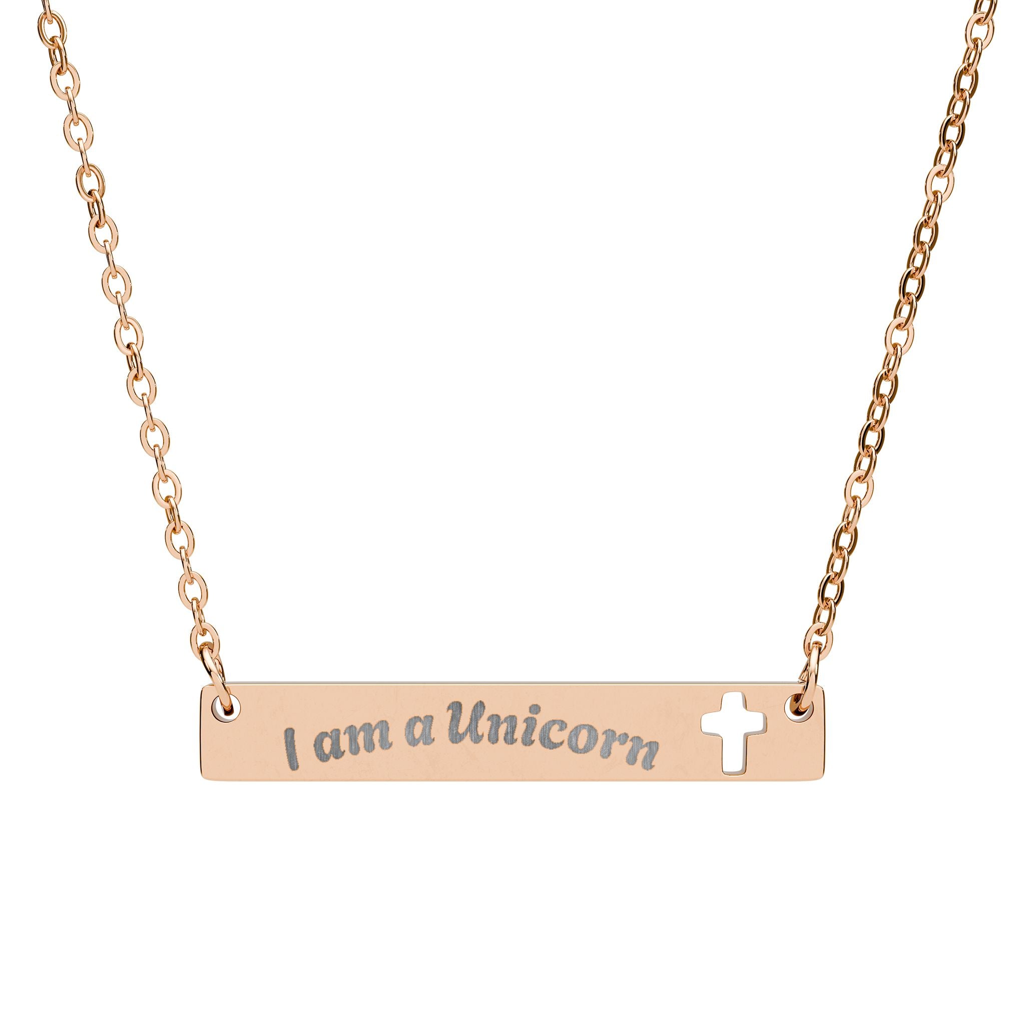 A rose gold bar necklace with the words 'I am a Unicorn' engraved on the bar, and a small open cross on the right side, shown against a plain white background.