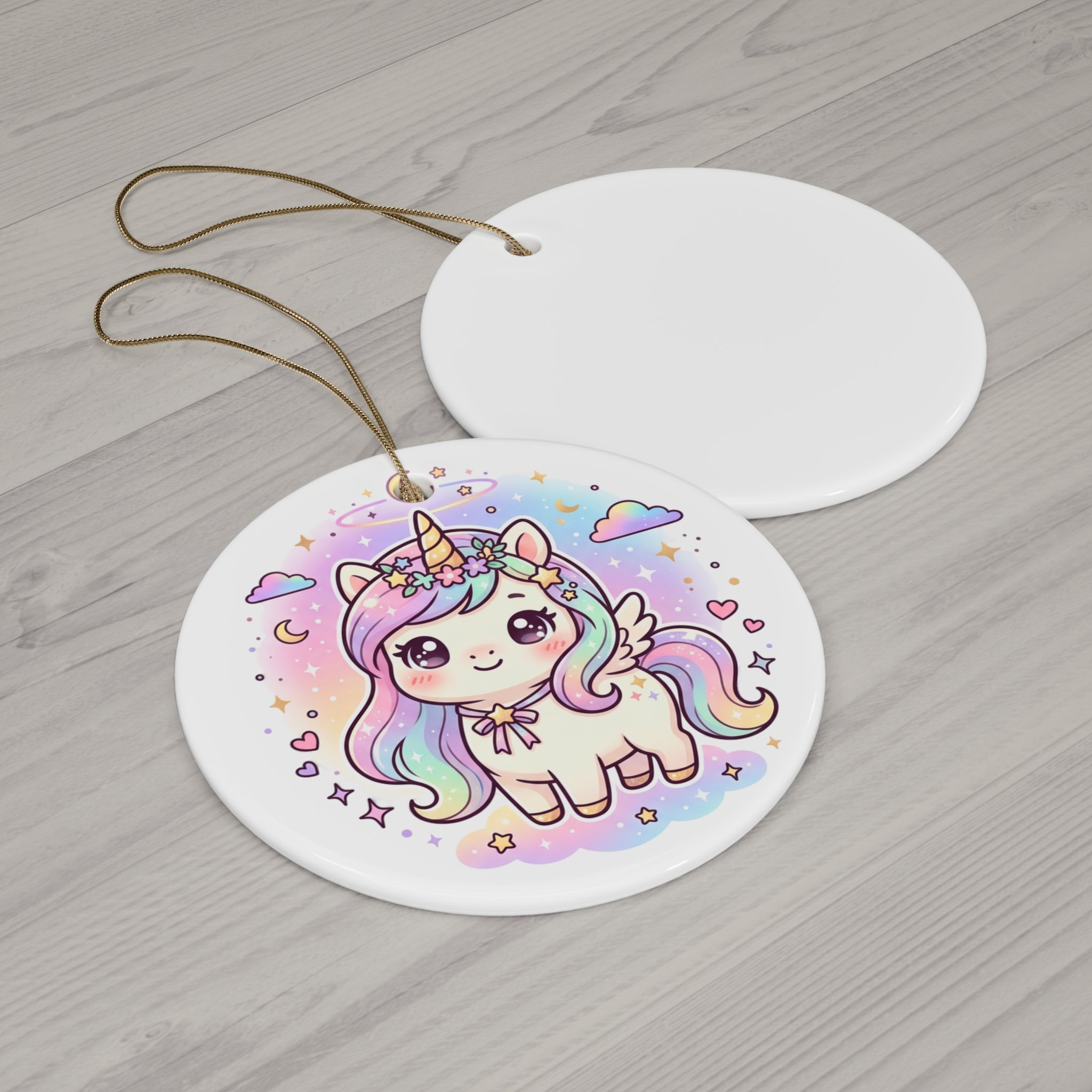 Two round white ceramic ornaments on a light gray wood background. The front ornament features a colorful illustration of a cute pastel unicorn with a rainbow mane, horn, and wing, surrounded by stars and clouds.