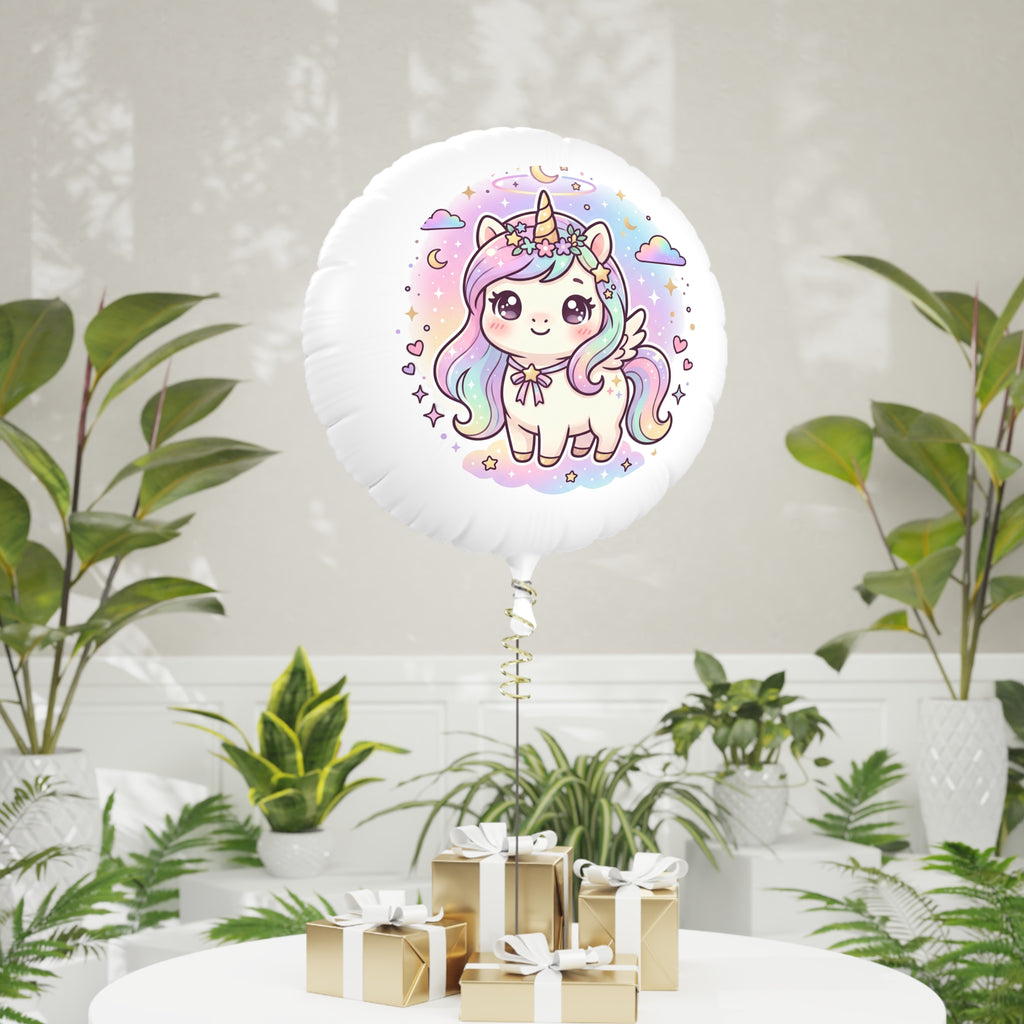 A round white foil balloon with a colorful cartoon unicorn illustration, standing on a table in a styled indoor setting with potted plants and small wrapped gifts.