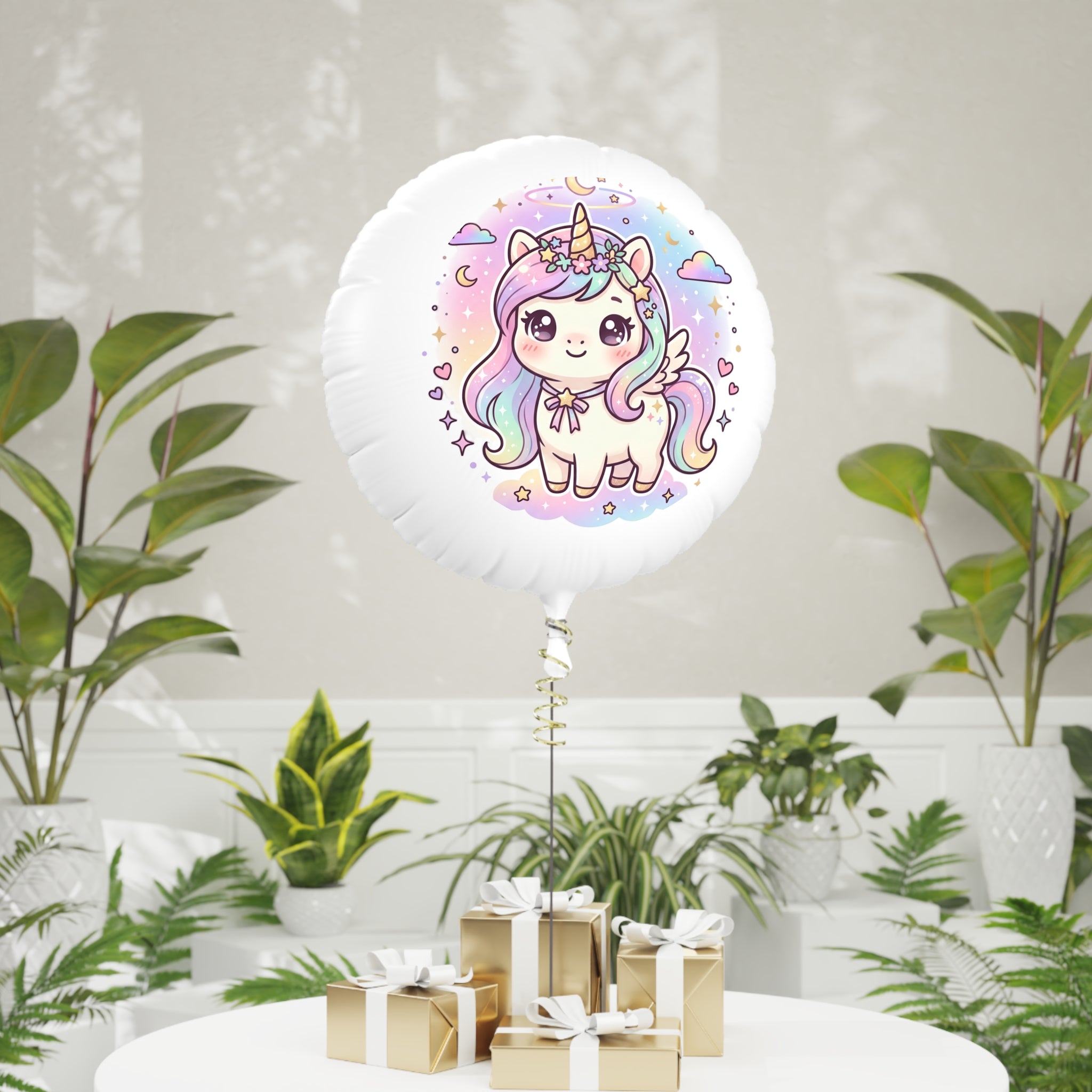 A round white foil balloon with a colorful cartoon unicorn illustration, standing on a table in a styled indoor setting with potted plants and small wrapped gifts.