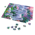 A completed colorful jigsaw puzzle showing a fantasy scene with two white unicorns in a flower-filled meadow, displayed on a white background with several loose puzzle pieces scattered around it.